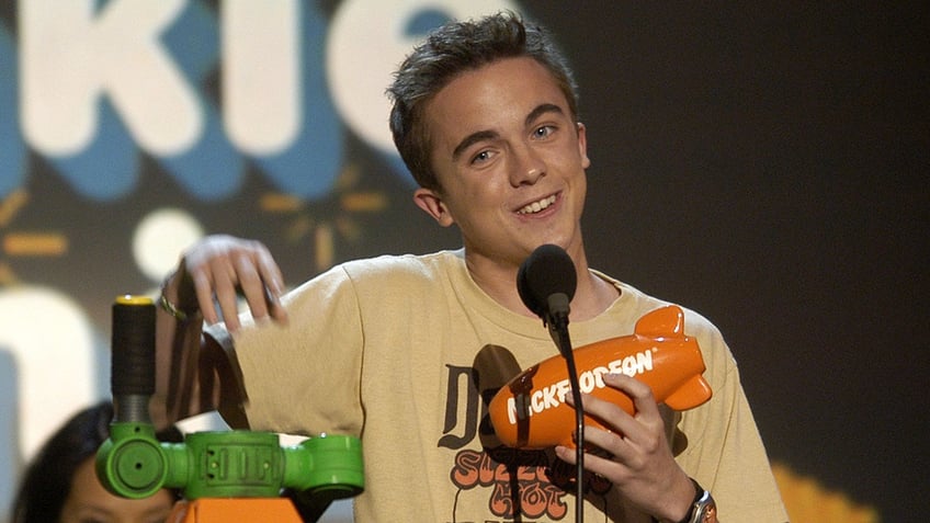 Frankie Muniz in a yellow/tan shirt smiles on stage at Nickelodeon's KIds' Choice Awards