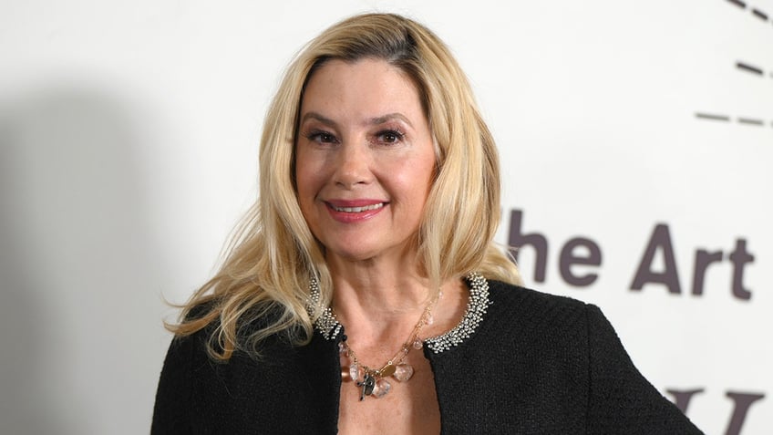 Mira Sorvino in a black jacket smiles for the camera on the carpet in Los Angeles