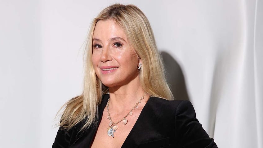 Mira Sorvino smiles wearing black blazer with ornate necklace