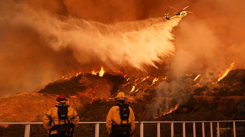 Firefighters watch as water is dropped on the Palisades Fire in Mandeville Canyon