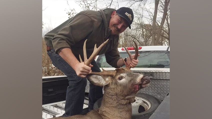 Man in pickup truck holding dead deer.