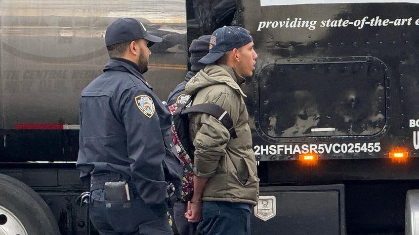 Migrant in handcuffs being led by NYPD police