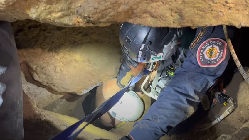 a close up shot of a man being pulled to safety after being trapped in a hole on a cliff