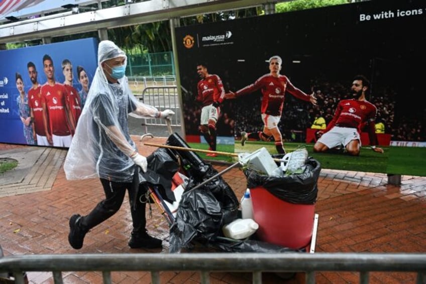 A man pushes a rubbish bin past posters of Manchester United players outside Hong Kong Sta