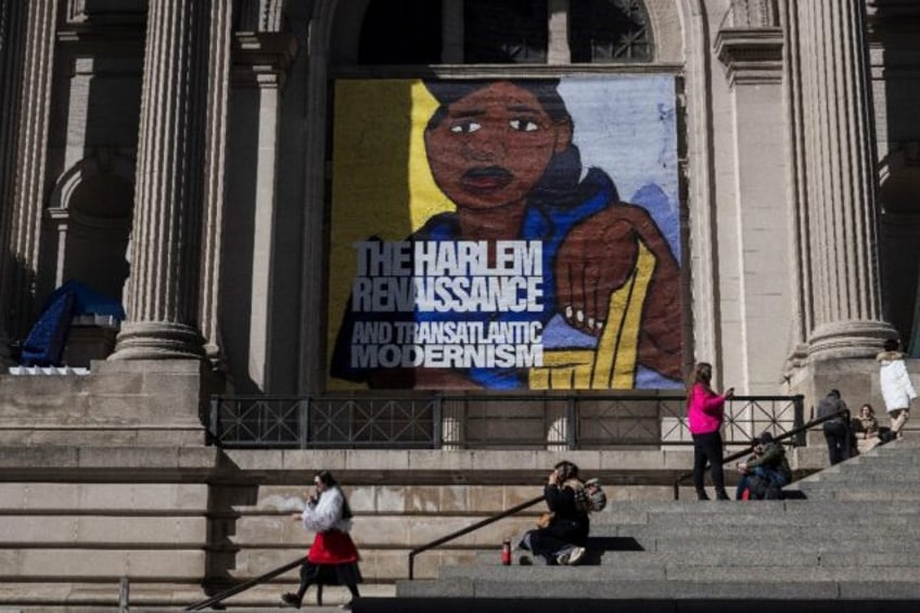 People sit on the stairs of The Metropolitan Museum of Art (The Met) in front of a poster