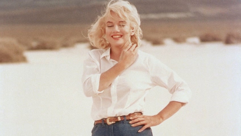 Marilyn Monroe smiling wearing a white t-shirt and blue jeans.