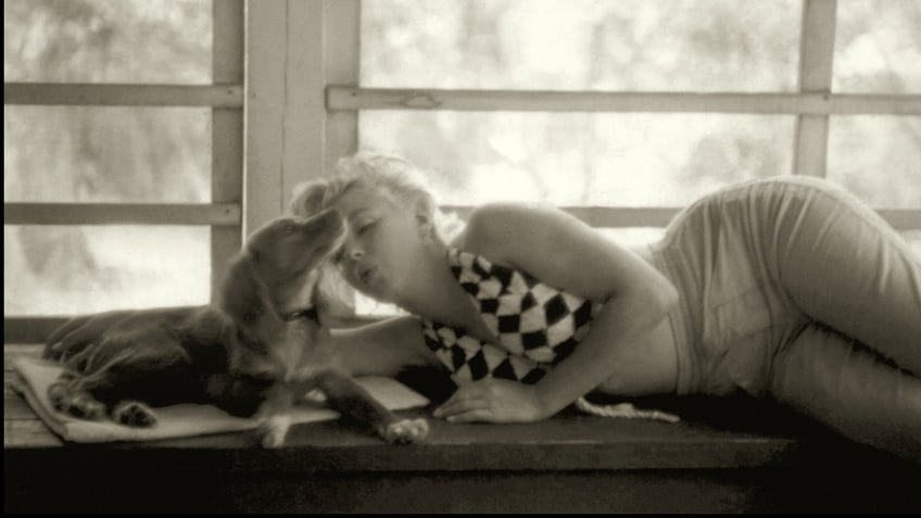 Marilyn Monroe receiving a kiss from a dog.