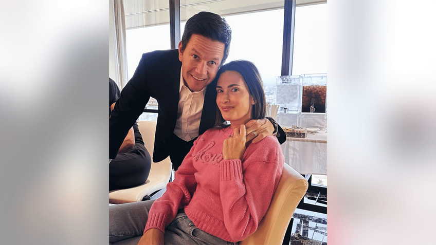 Mark Wahlberg in a black suit puts his arm around a seated Rhea Durham in a pink sweater