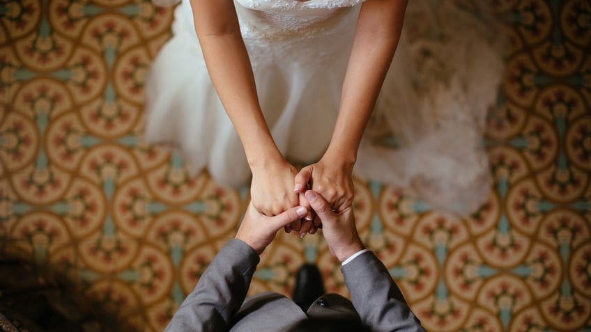 A close up shot of a bride and groom holding hands from a top view.