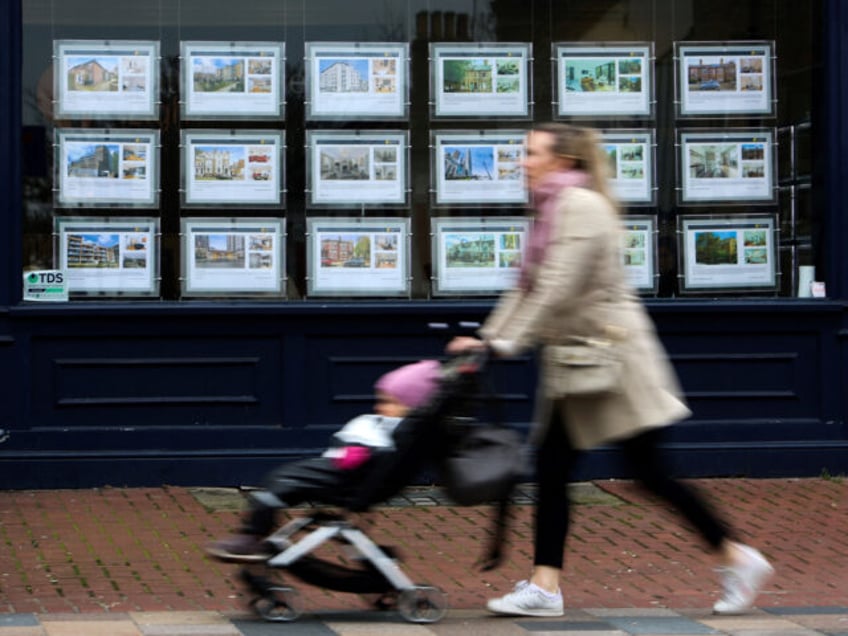 Pedestrians walk past the front window of an estate agent advertising properties to let an