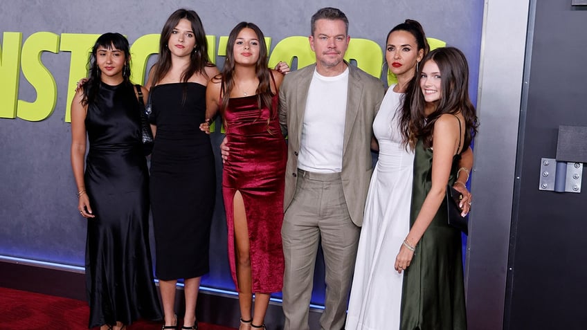 Alexia Barroso in a black dress stands next to sister Isabella Damon, also in black, next to Gia Damon in a red dress, next to Matt Damon in a sand-colored suit, next to wife Luciana in a white gown next to daughter Stella in a green dress on the red carpet