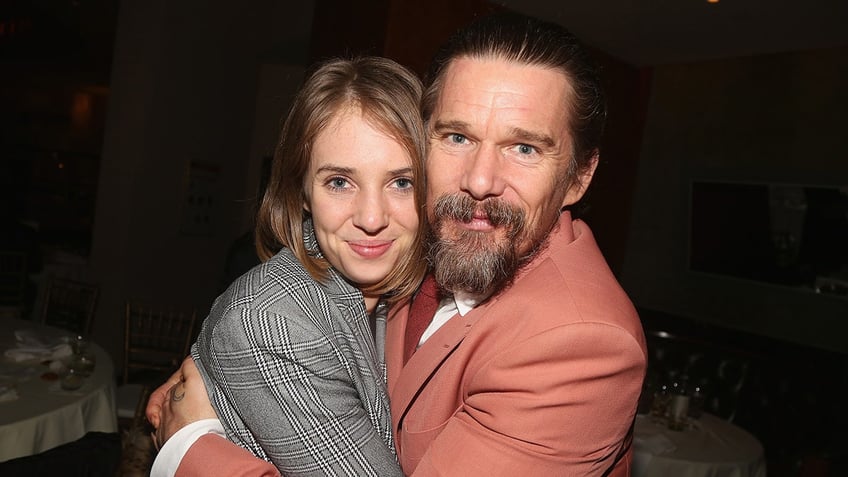 Maya Hawke in a plaid jacket hugs her father Ethan in a salmon jacket tightly