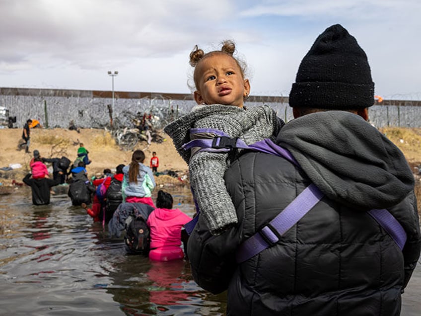 A migrant man crosses the Rio Grande holding his child in the air to prevent her from gett