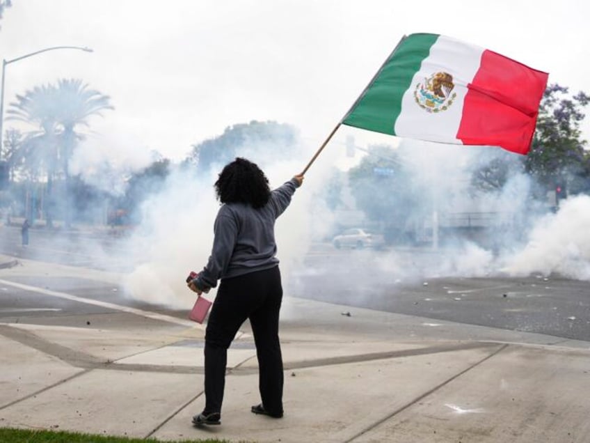 A woman waves a Mexican flag amidst tear gas from law enforcement during a protest in Para