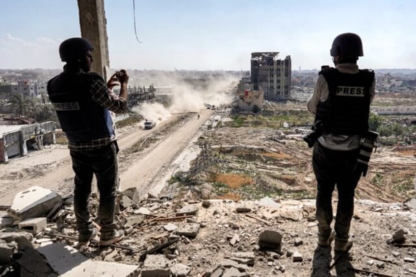 Journalists film from atop a damaged building facing the ravaged Al-Salam hospital in Khan