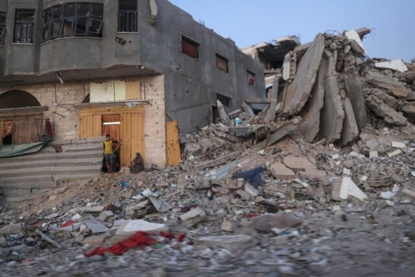 Palestinians sit by a damaged building surrounded by rubble at al-Bureij camp in the centr