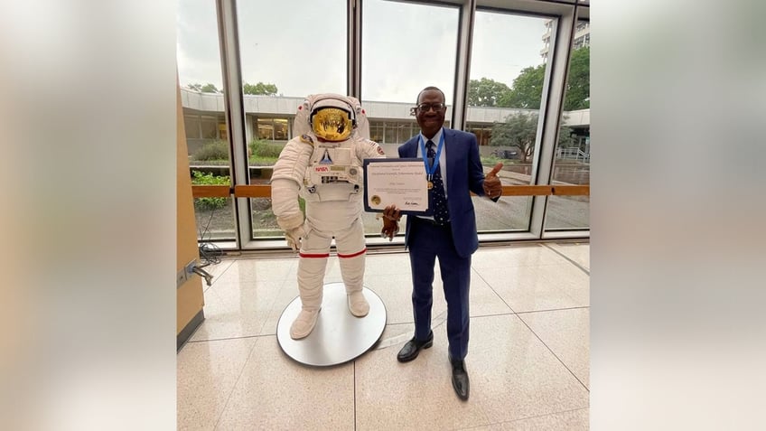 Dr. Zubair displays his NASA medal for Exceptional Scientific Achievement next to a statue of an astronaut.