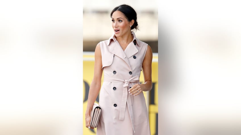 Meghan Markle looking surprised outdoors wearing a sleeveless beige suitdress