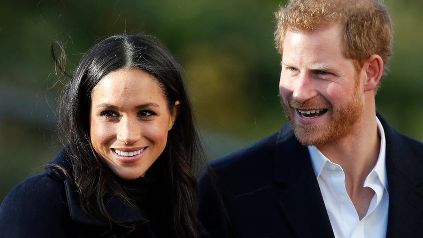 A close-up of Meghan Markle and Prince Harry walking together and smiling outdoors.