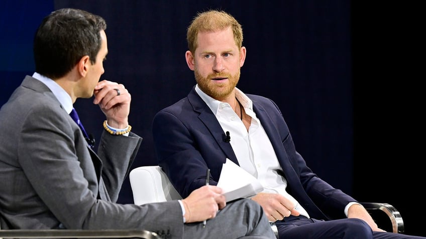 Prince Harry in a navy blazer speaks on stage at The New York Times DealBook Summit