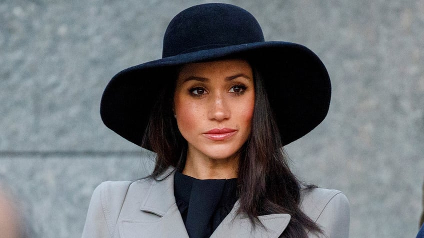 Meghan Markle wearing a grey blazer, a black shirt and an oversized black hat.