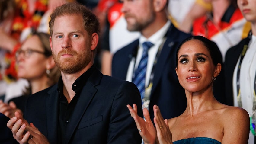 A close-up of Prince Harry and Meghan Markle applauding with an audience.