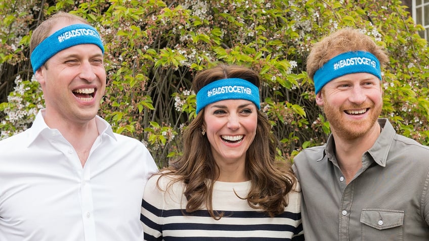 Prince William, and Prince Harry smiling wearing matching blue headbands outdoors.