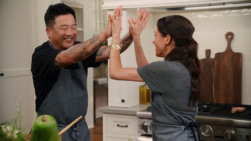 Meghan Markle giving high-five to a man wearing a matching grey shirt.