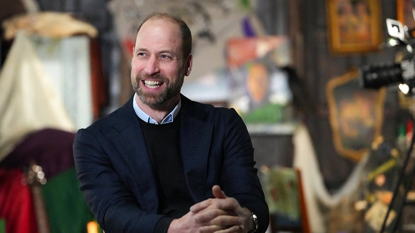 Prince William smiling in a blue blazer and black sweater