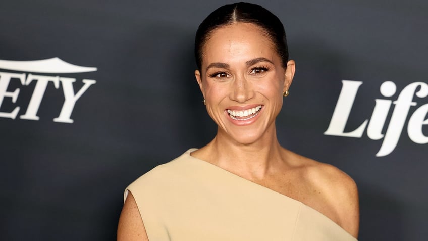 Meghan Markle smiles in one shoulder tan dress