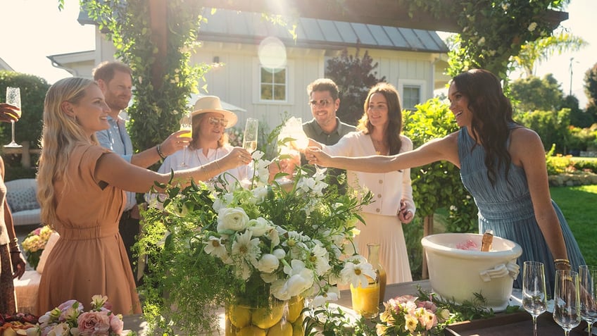 Prince Harry and Meghan Markle with friends toasting at a garden.