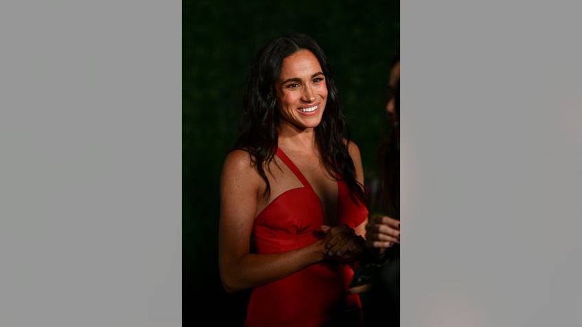 Meghan Markle smiling and wearing a red strappy dress.