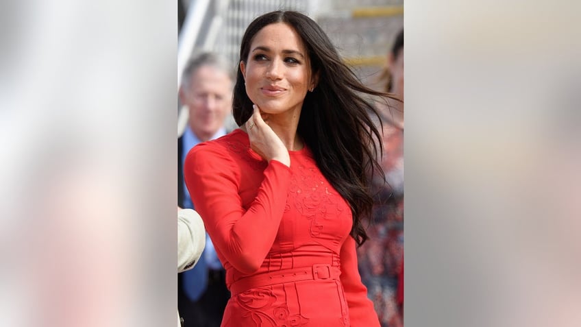 Meghan Markle smirking and wearing a fitted red dress.