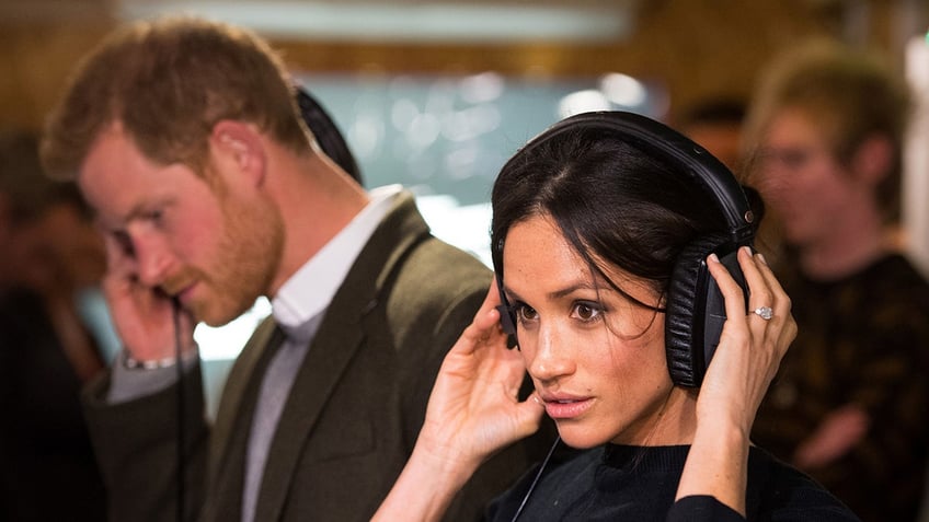 Meghan Markle and Prince Harry listening to headphones.