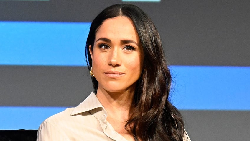 Meghan Markle looking serious in a beige blouse.