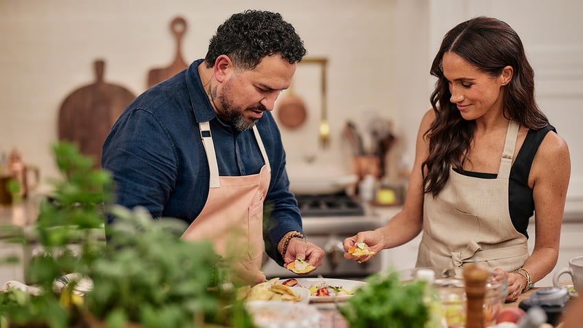 Meghan Markle cooking with a chef wearing an apron at a California kitchen