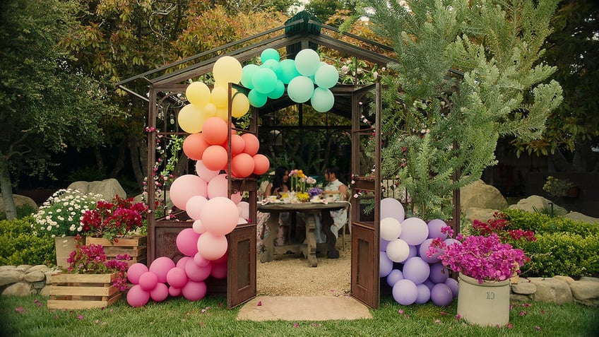 Meghan Markle and Mindy Kaling sitting down and having a tea party surrounded by balloons.