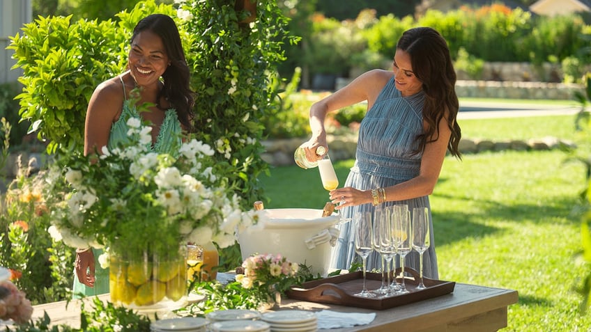 Meghan Markle outdoors serving bellinis next to a smiling friend.