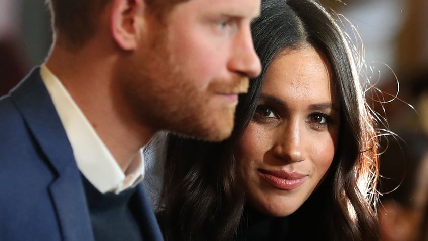 Meghan Markle looking directly at the camera as Prince Harry looks away