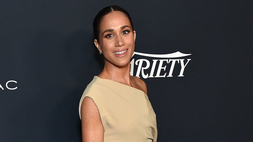 A close-up of Meghan Markle wearing a beige off the shoulder dress