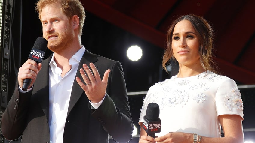 Meghan Markle looking serious standing next to Prince Harry as he speaks