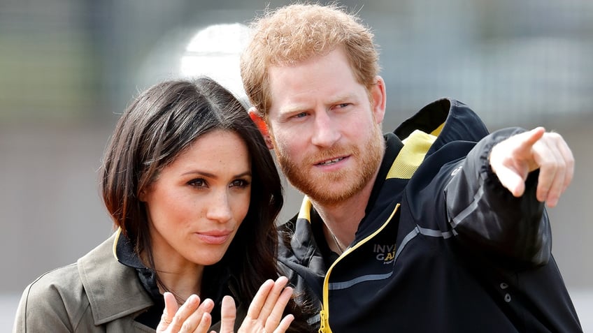 Prince Harry pointing as Meghan Markle looks on.