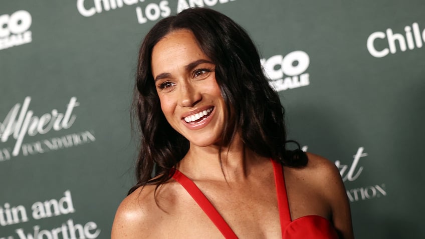 A close-up of Meghan Markle smiling wearing a plunging red dress.