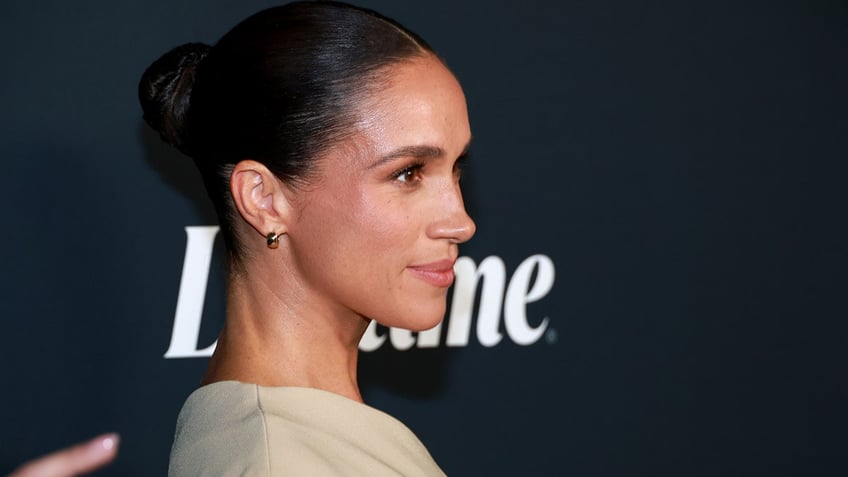 A close-up of Meghan Markle posing to the side at a Lifetime TV event wearing a beige dress