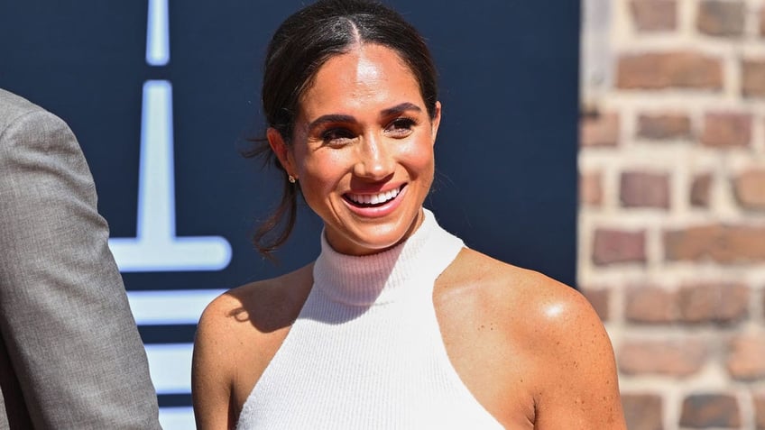 Meghan Markle smiles in a white halter top