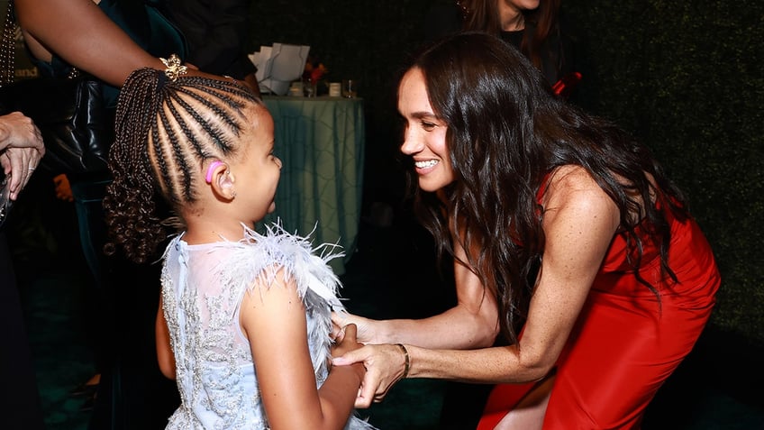 Meghan Markle holding the arms of a little girl and smiling.