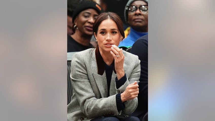 Meghan Markle sitting down and wearing a grey blazer.