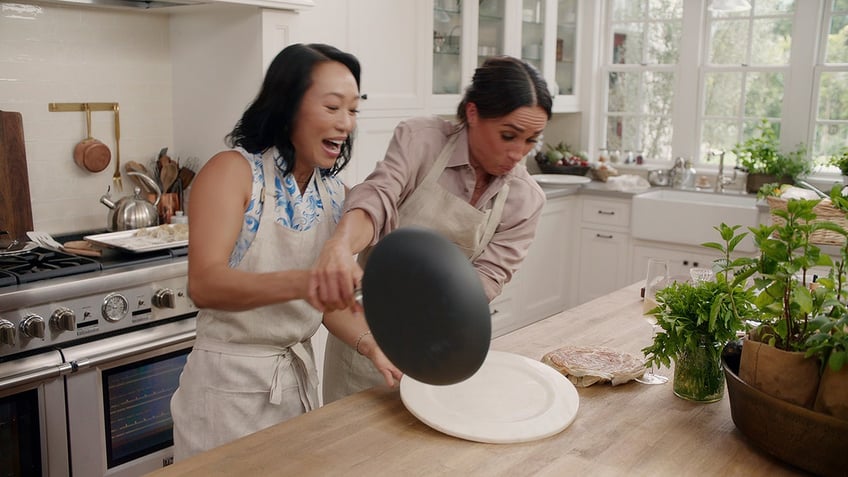 Meghan Markle and a friend in a kitchen laughing trying to cook.