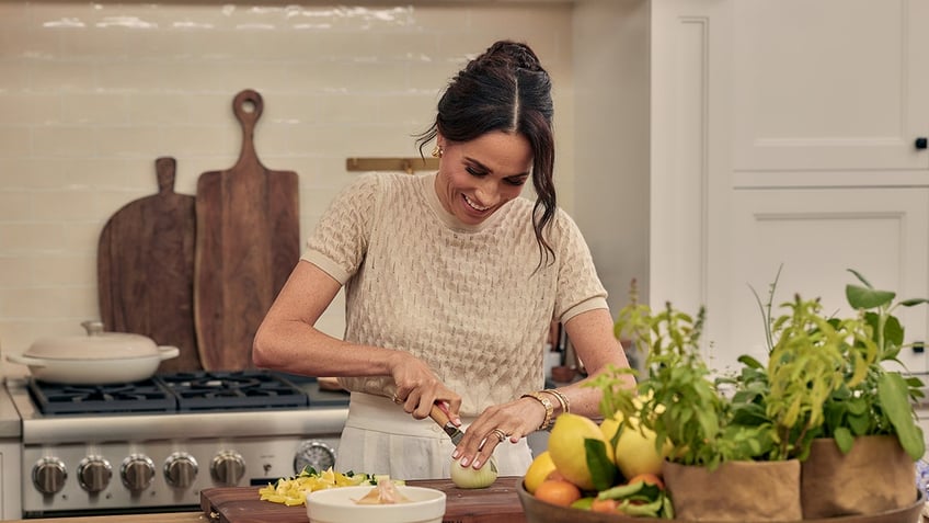 A close-up of Meghan Markle smiling and tending to fruits and vegetables in her kitchen.