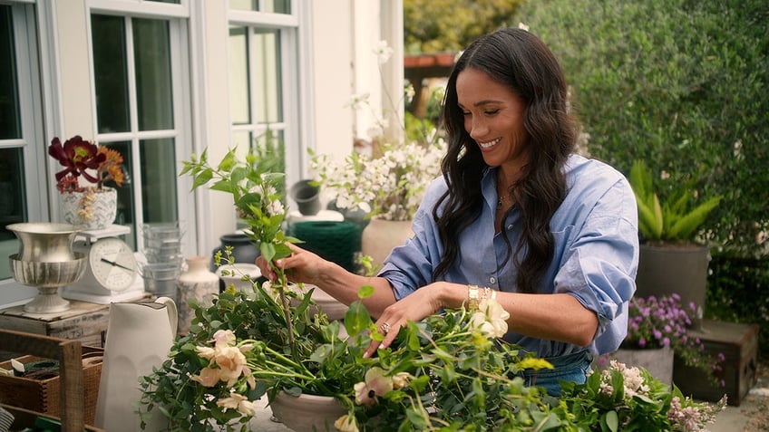 Meghan Markle wearing a blue shirt and smiling while tending to her garden.